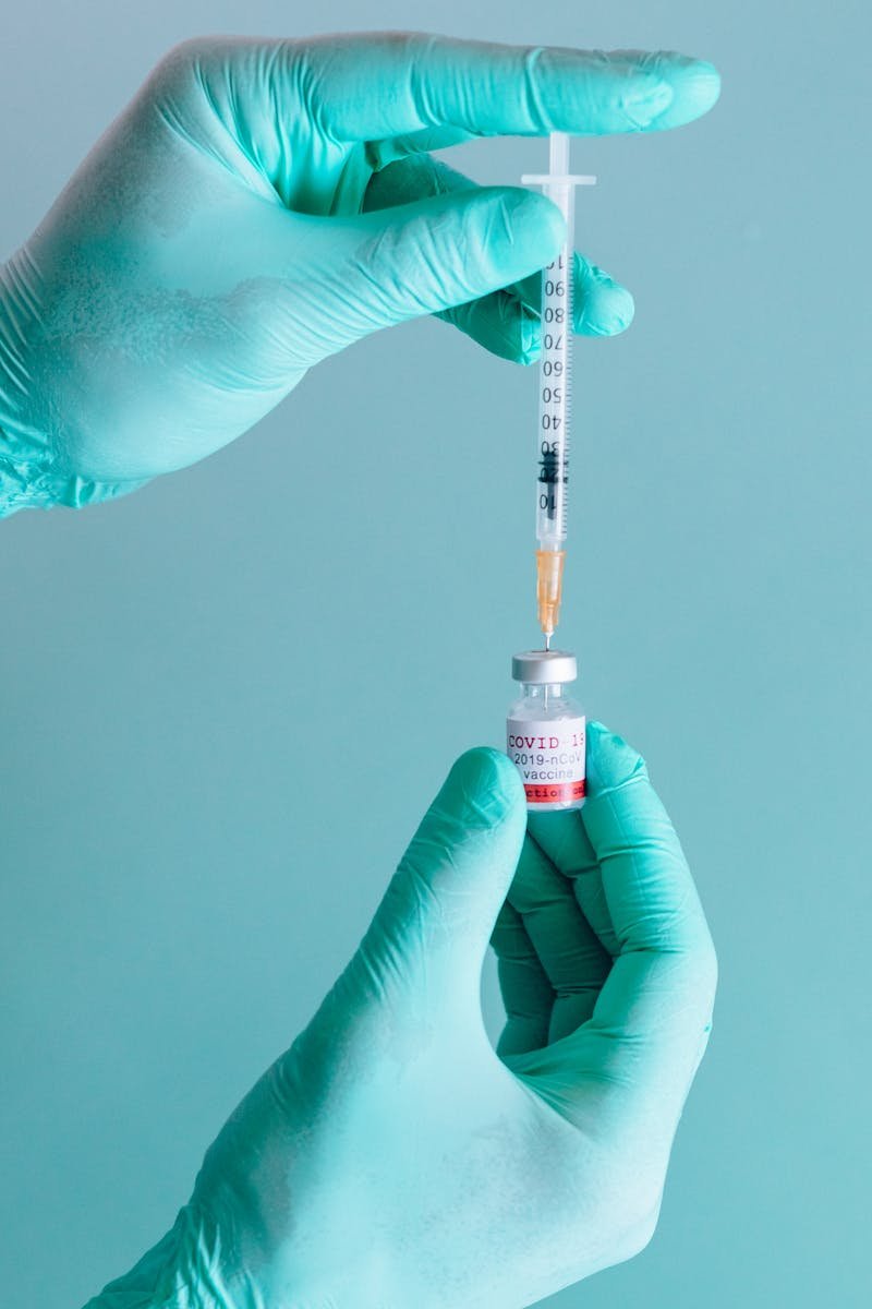 Healthcare worker holding syringe and vial for COVID-19 vaccination on teal background.